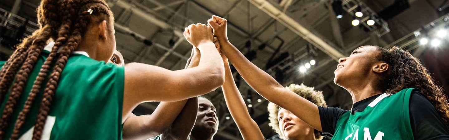 In a sports complex, uniformed team members join their raised arms in a gesture of solidarity.