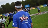 A boy walks on a football field where other players are already practicing